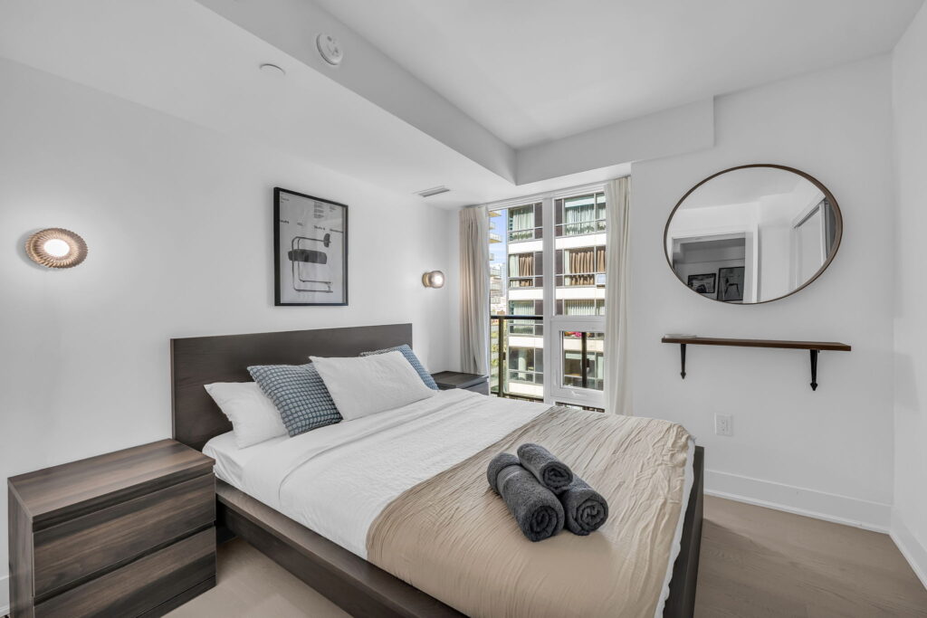 Staged bedroom with queen bed and round mirror in a Certus-managed rental at 955 Bay St
